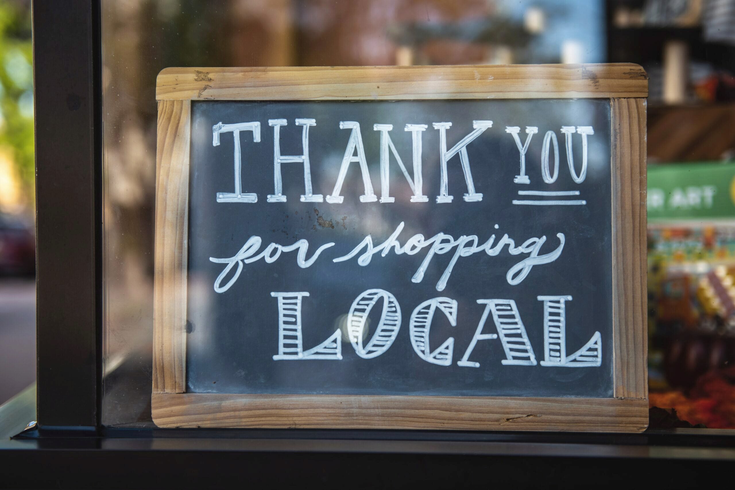 A chalkboard sign with the message "Thank you for shopping local" written in white, set in a wooden frame.