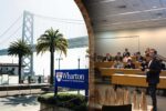 The image is a split scene. On the left, there are palm trees with the Bay Bridge in the background and a sign for the Wharton School of the University of Pennsylvania. On the right, a classroom setting with students and an instructor is visible
