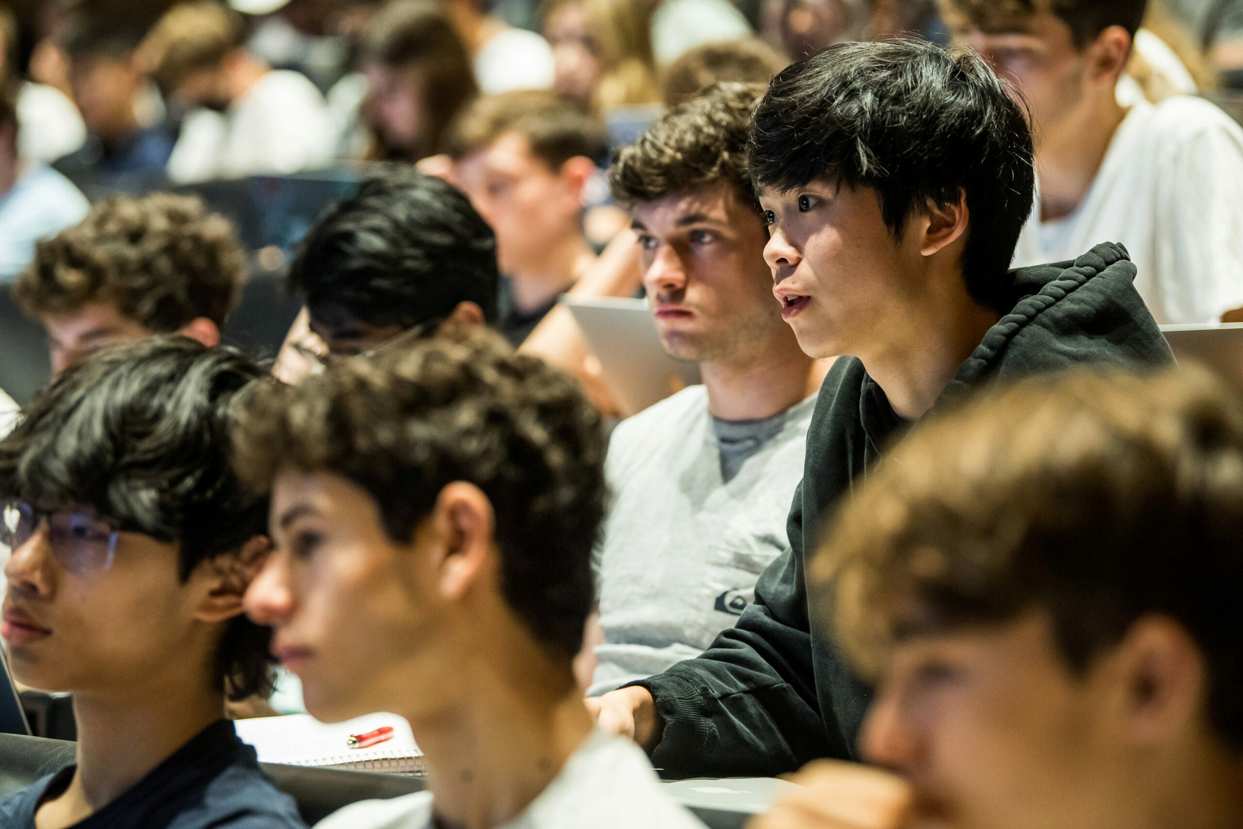 A diverse group of students attentively listens and takes notes in a lecture hall.