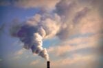 A factory smokestack emitting large clouds of smoke against a sky, representing industrial pollution.
