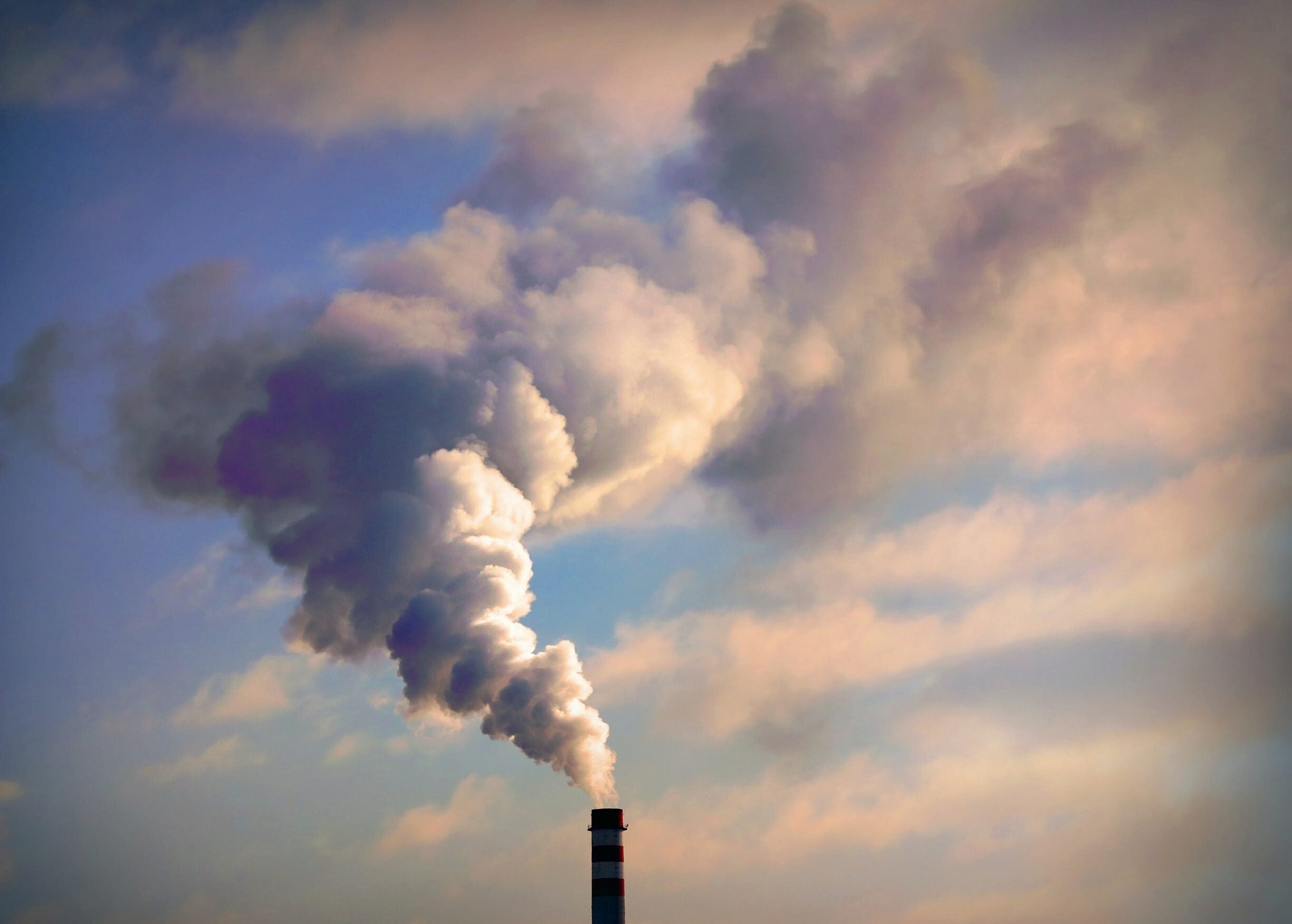 A factory smokestack emitting large clouds of smoke against a sky, representing industrial pollution.