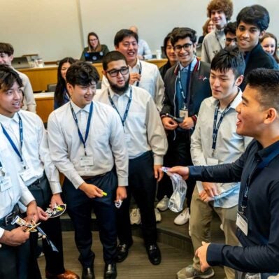 A group of young people in a classroom setting, wearing lanyards, engaged in a lively discussion or activity.