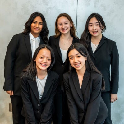 Five people dressed in black suits, smiling and posing together in a group photo.