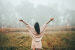 A person standing with arms outstretched in a misty field, conveying a sense of freedom and connection with nature.