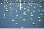 Tennis court with numerous bright yellow tennis balls scattered across the surface.