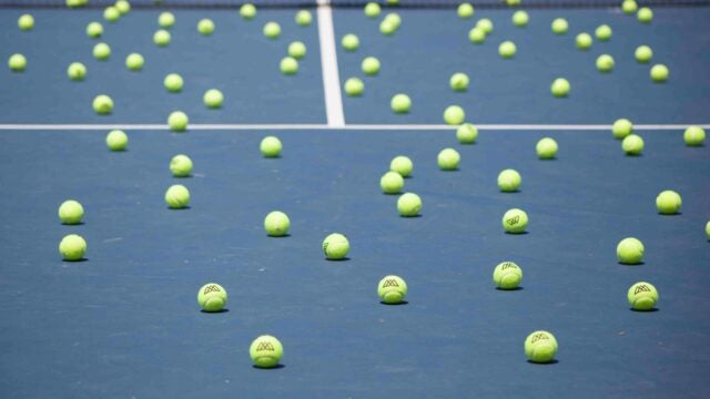 Tennis court with numerous bright yellow tennis balls scattered across the surface.