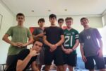 A group of young people poses indoors, some with casual gestures. They are wearing a mix of athletic and casual clothing. The room has modern decor.