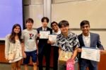 A group of young adults standing together, some holding certificates, possibly celebrating their participation and achievement in a program related to entrepreneurship. They appear happy and are in a classroom setting with a projector screen in the background.