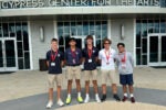 A small group of individuals standing in front of a building labeled "Cypress Center for the Arts." They are wearing casual attire with lanyards and name tags.