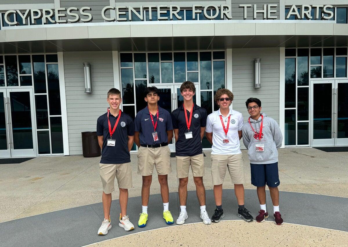 A small group of individuals standing in front of a building labeled "Cypress Center for the Arts." They are wearing casual attire with lanyards and name tags.