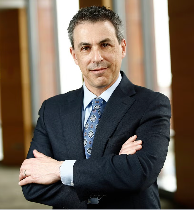 man in blue suit jacket and blue tie, white shirt with arms crossed looking at the camera