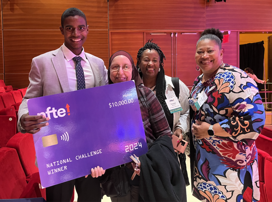 A young man holding a big $10,000 check from the network for teaching entrepreneurship alongside three women Los Angeles Urban League teachers.