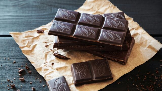 Dark chocolate bars with cocoa leaf designs on top, stacked on brown paper with chocolate shavings scattered around.