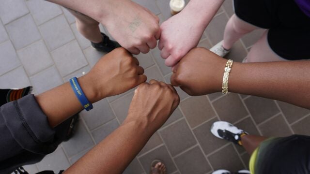 Several people forming a fist bump circle, symbolizing unity and teamwork, standing on a tiled floor.