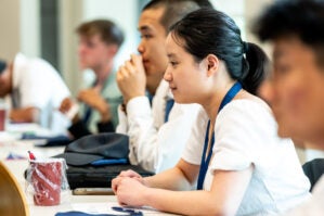 250425 Wgyp Invest 1182 A group of people sitting attentively in a classroom setting, wearing lanyards, and appearing engaged in a lecture or discussion.