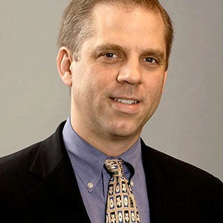 Headshot of person wearing a suit, shirt, and patterned tie.