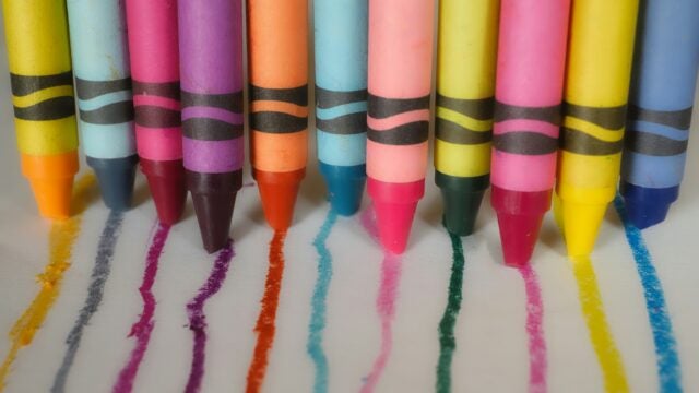 A row of colorful crayons with matching lines of color drawn on paper.